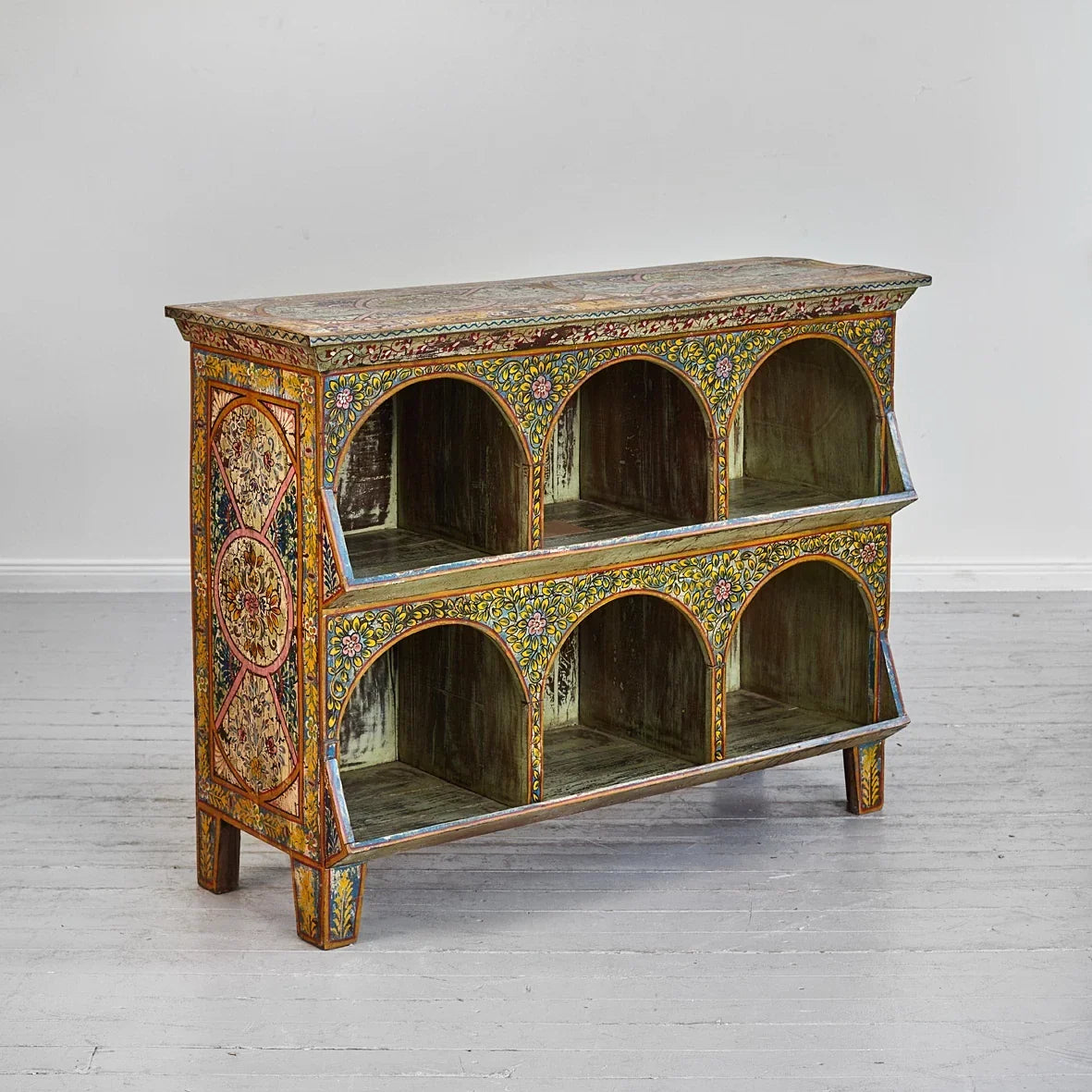 Decorative wooden cabinet with intricate patterns on a gray floor and white wall background