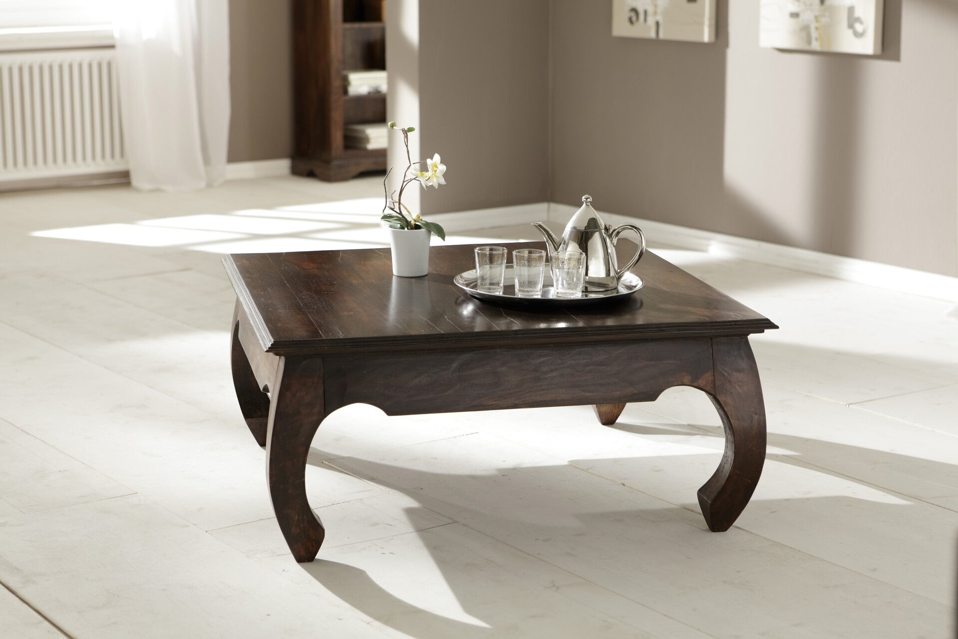 Square solid rosewood coffee table with curved opium legs in a modern living room.