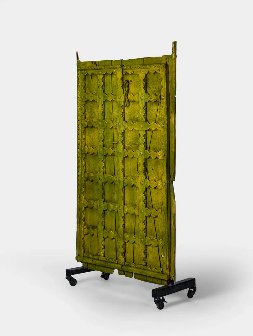Unique Marwari wooden door with iron stand, distressed olive green finish, 94 × 171 cm.

Handcrafted solid wood Marwari door panel with grid pattern and castor base.

Tall antique-style Indian door decor in olive green, made in India.