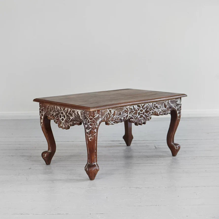 Ornate carved wood coffee table with scrolled feet and vine detailing.

