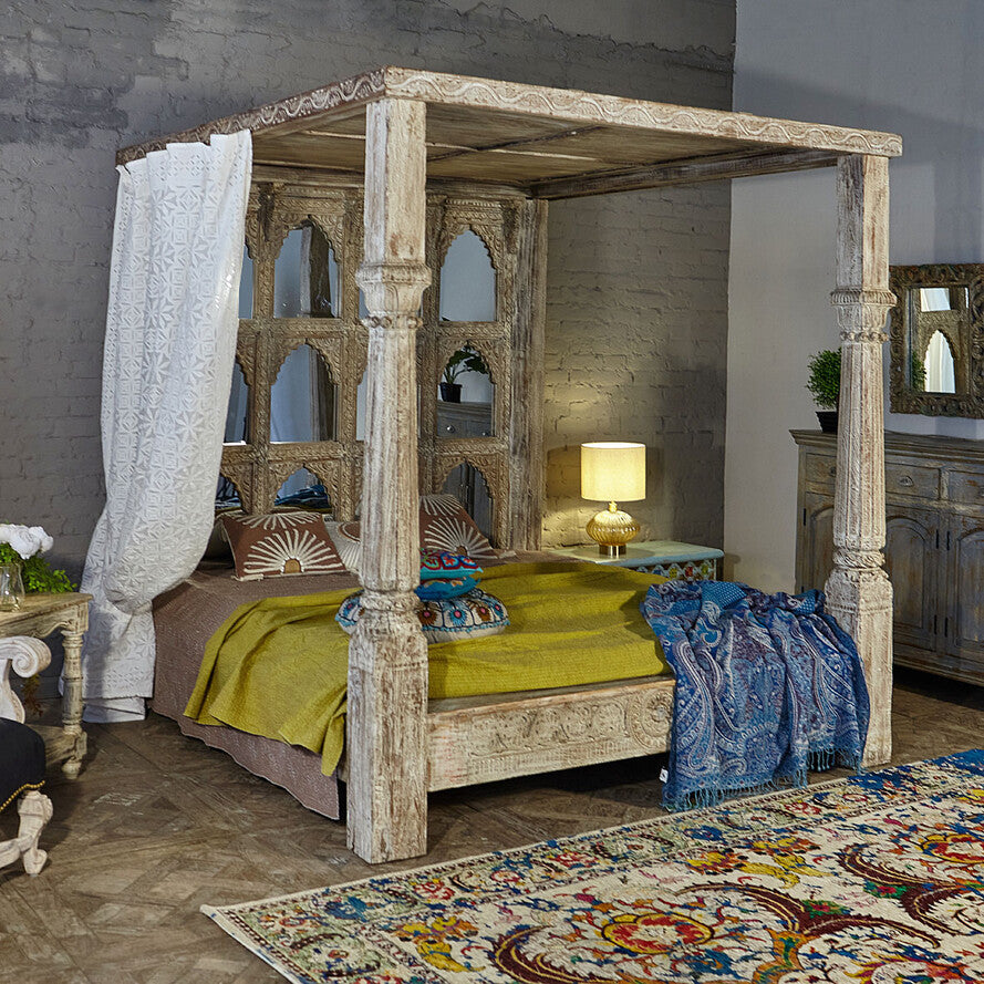 Wooden four-poster bed in a bedroom with decorative rug and furniture.