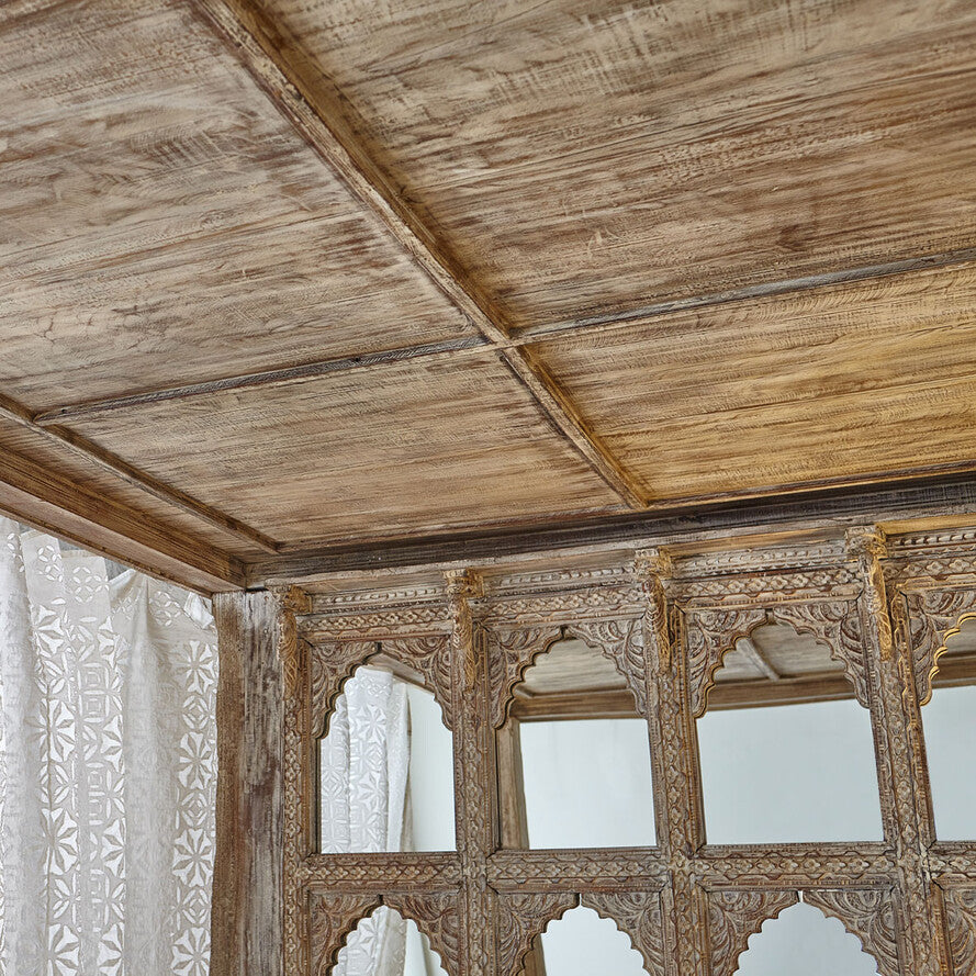 Wooden ceiling with intricate carvings and a window with white curtains.