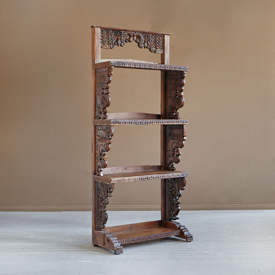 Wooden bookshelf with intricate carvings against a plain wall