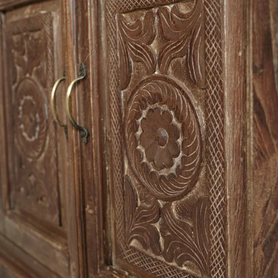 Close-up of a wooden cabinet with intricate carvings and a brass handle.