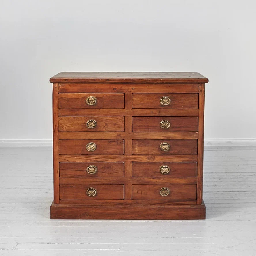 Wooden dresser with multiple drawers and brass handles on a light gray background