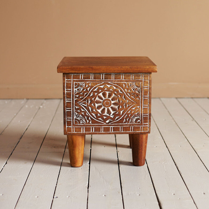 Wooden side table with decorative carvings on a wooden floor.