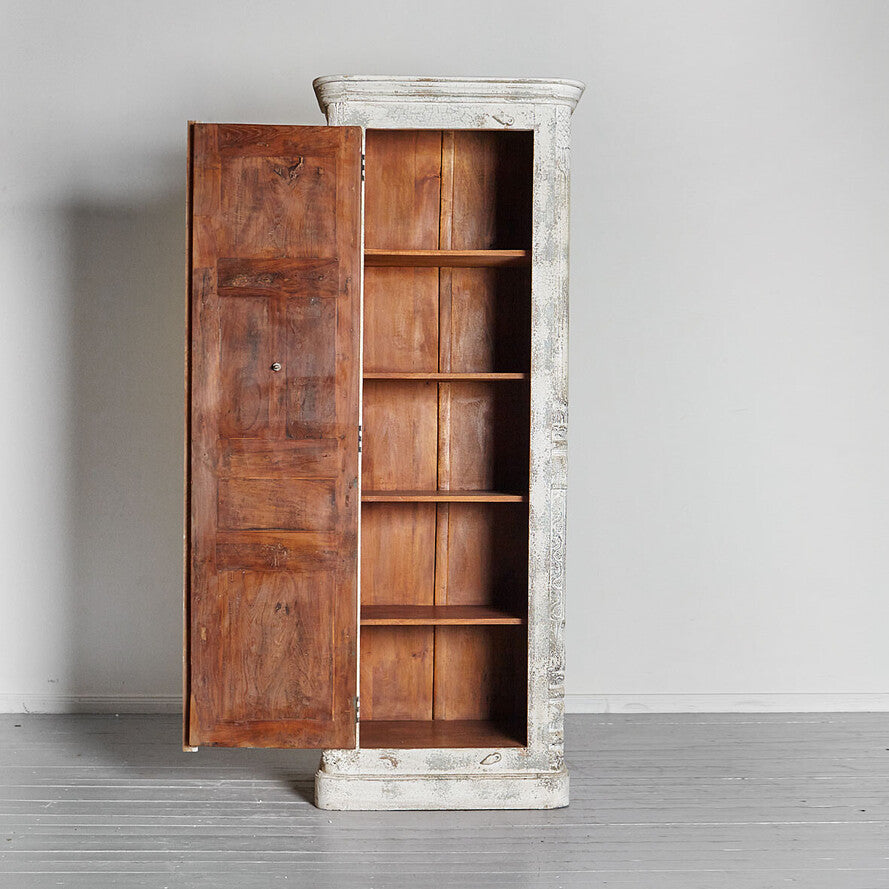 Wooden cabinet with distressed white top on a gray floor and background