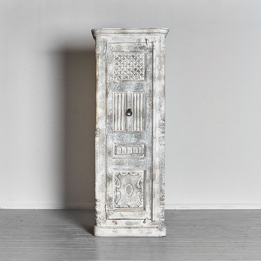 Decorative wooden cabinet with white distressed finish against a plain wall.