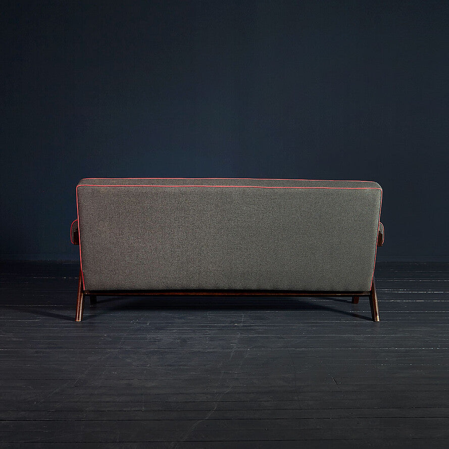 Gray sofa with red trim on a dark wooden floor and background