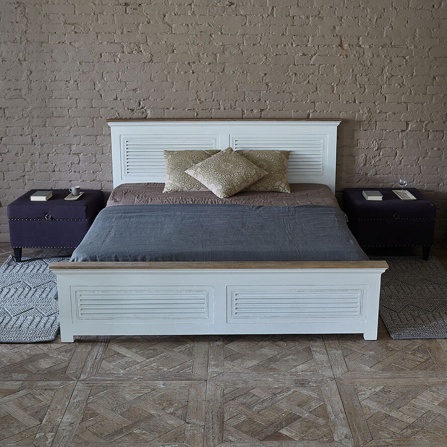 Bedroom with a white wooden bed frame, gray bedding, and two side tables against a brick wall.