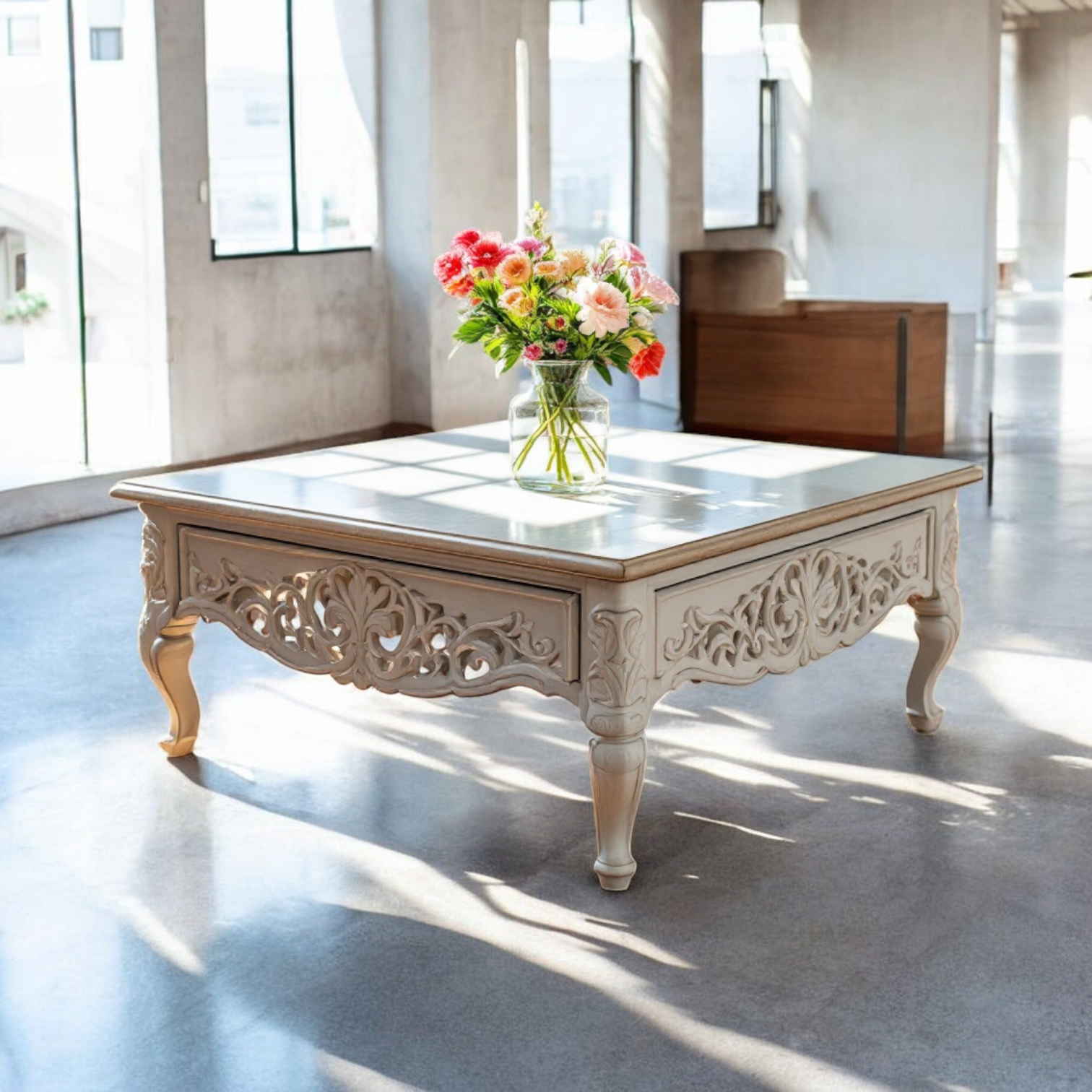 An antique wood coffee table with intricate carvings, placed in a room with natural lighting and a vase of flowers on top.