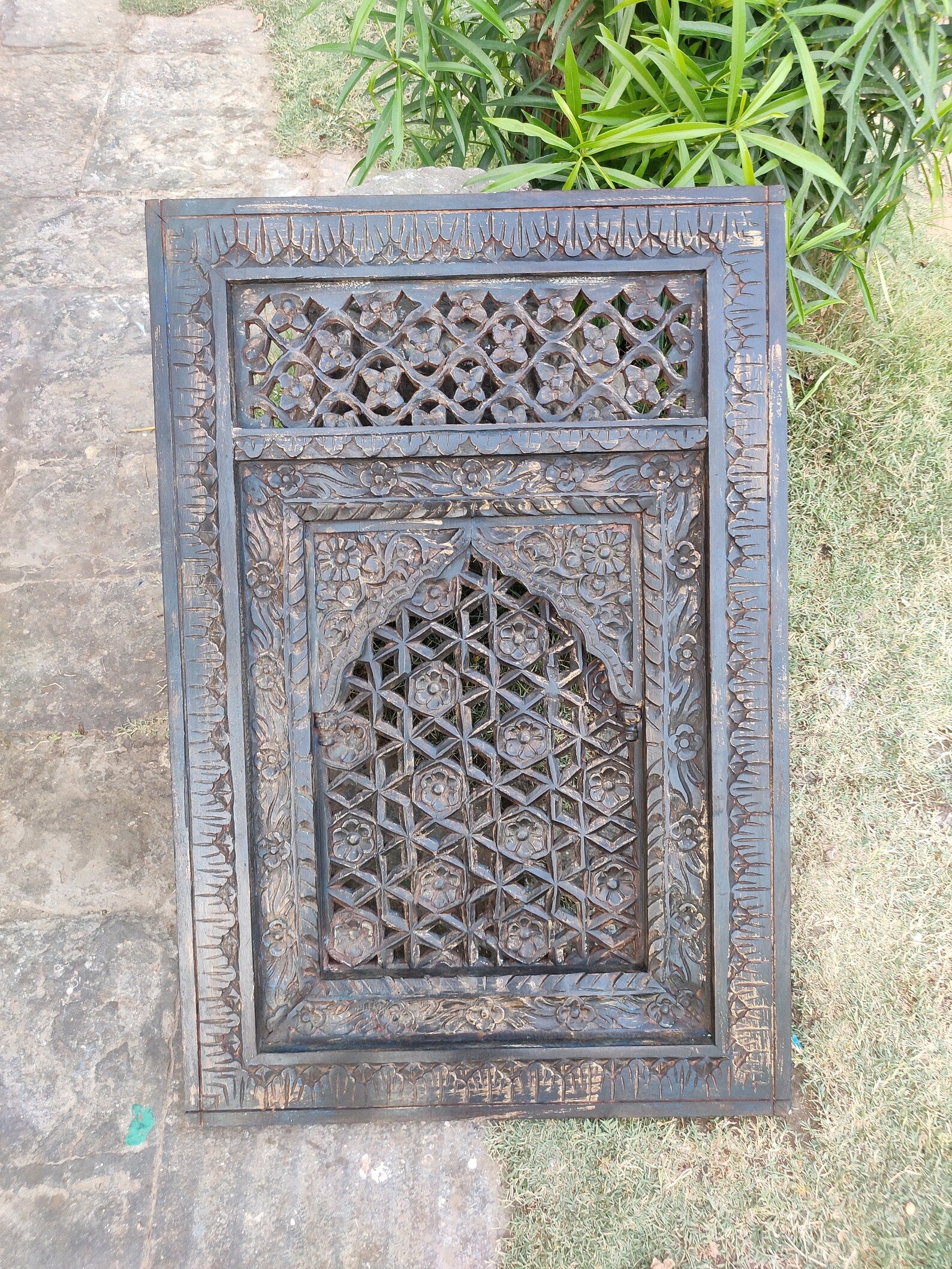 Decorative metal grille with intricate patterns on a stone and grass background