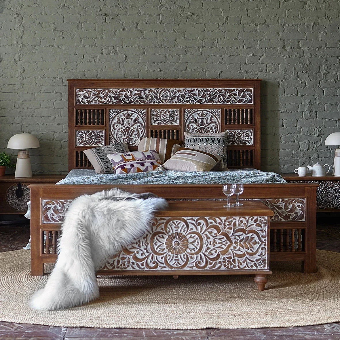 Wooden bed with intricate carvings against a textured wall.