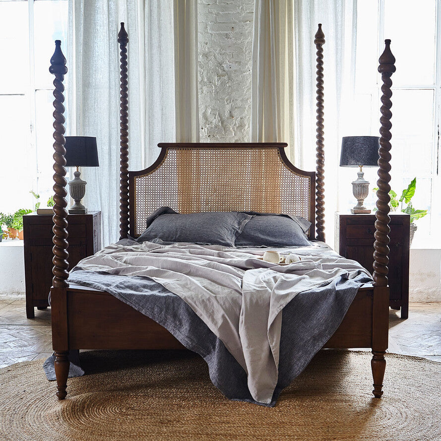 Four-poster bed with wooden frame and caned headboard in a bright bedroom.