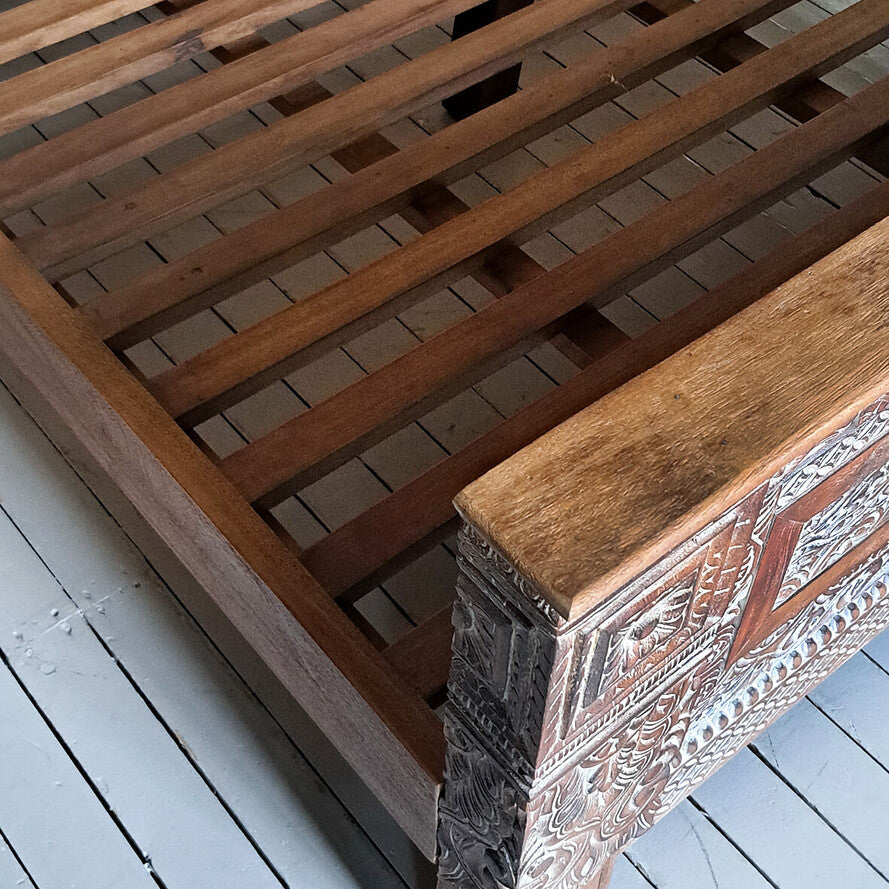Wooden bed frame with intricate carvings on a light wooden floor.