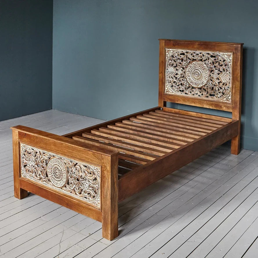 Wooden bed with intricate carvings on a gray floor and wall.
