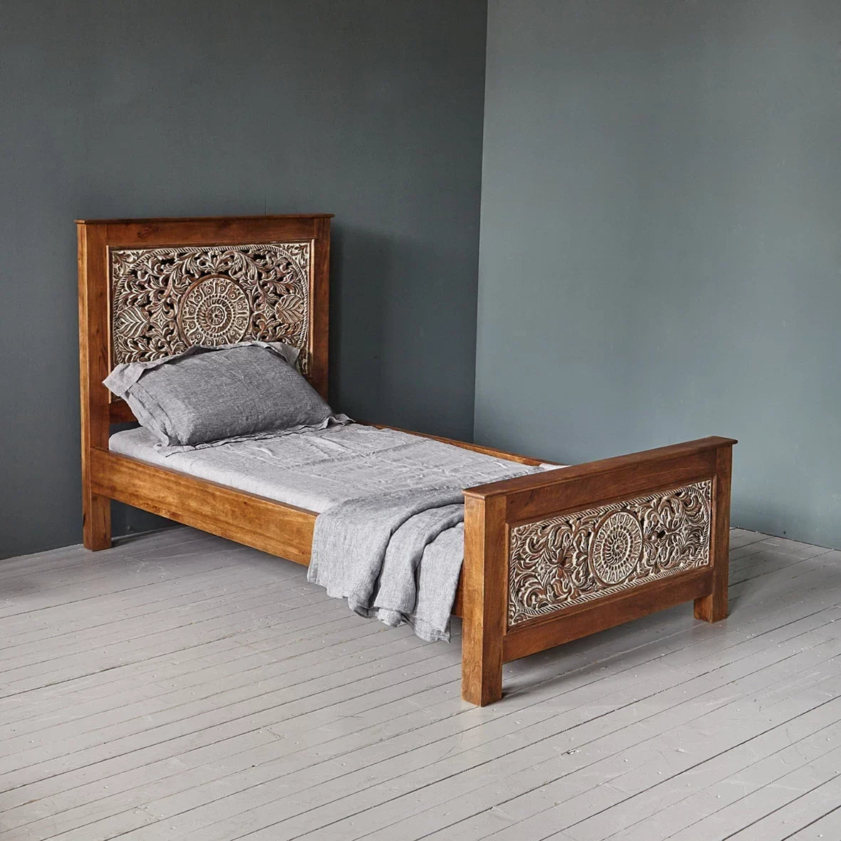 Wooden bed with intricate carvings against a gray wall