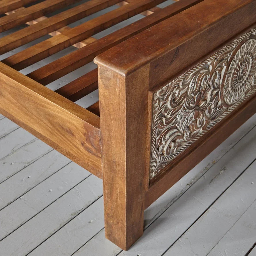 Wooden bed frame with intricate carvings on a wooden floor