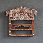 Decorative wooden wall hook with intricate carvings on a gray wall.