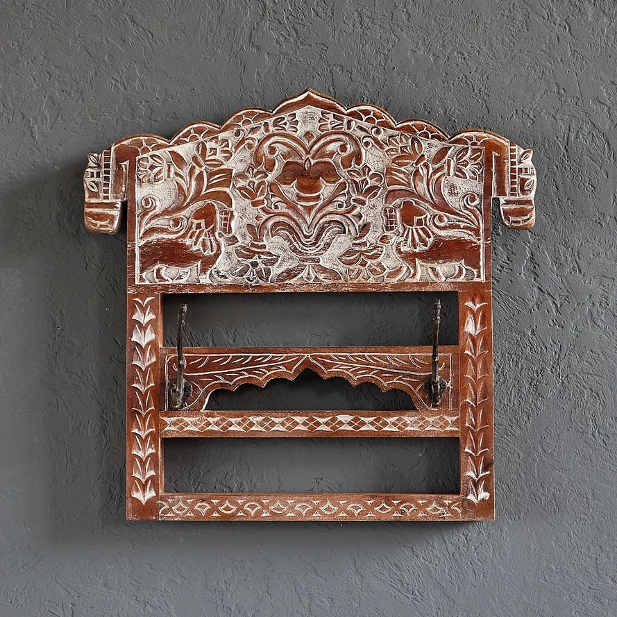 Decorative wooden wall hook with intricate carvings on a gray wall.
