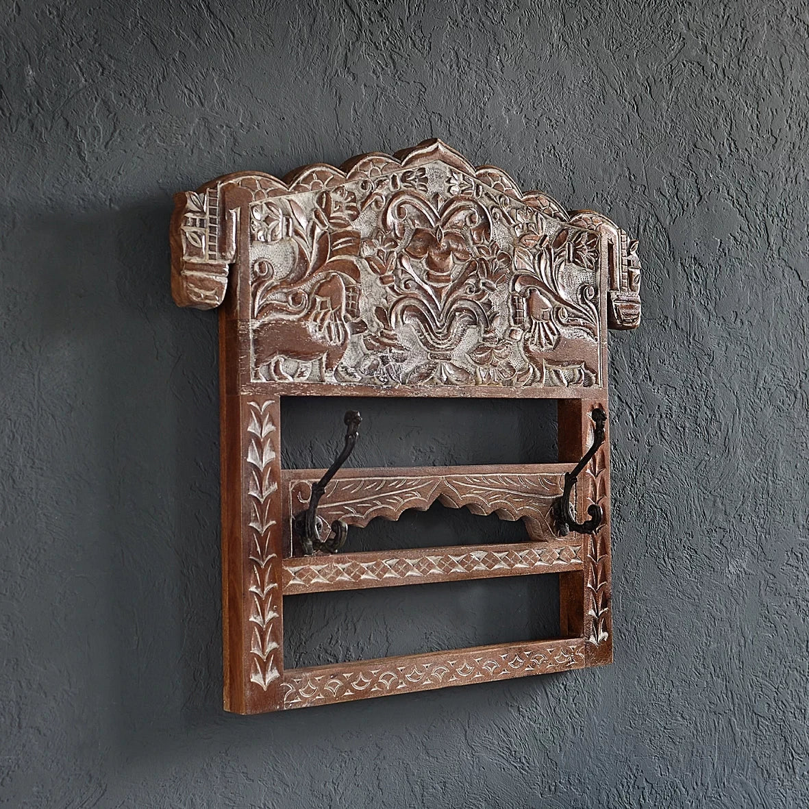Decorative wooden wall shelf with intricate carvings on a dark gray wall.